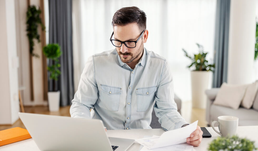 Man in glases holding papers on laptop