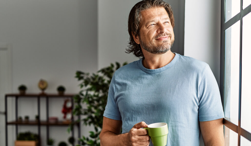 man looking out window with coffee